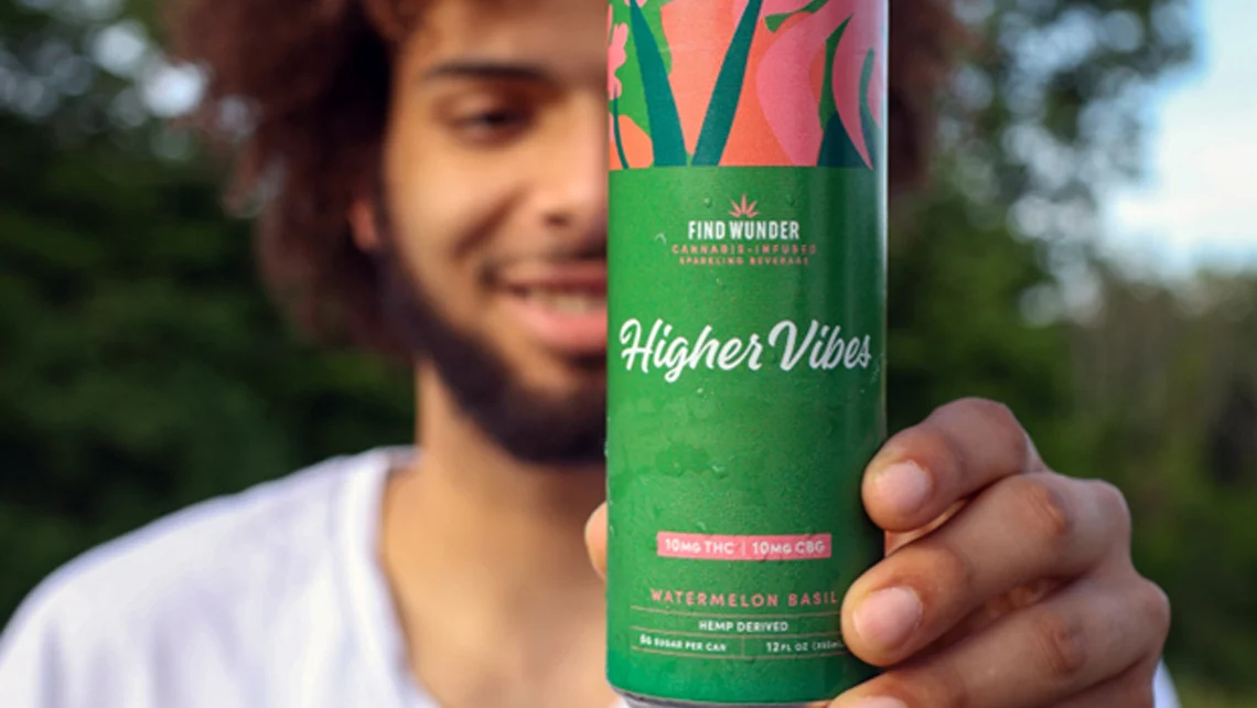 A man with a beard and curly hair holding a can of Wunder Higher Vibes Watermelon Basil