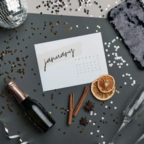 January calendar surrounded by disco ball, champagne glasses, pouch, wine bottle, oranges, cinnamon