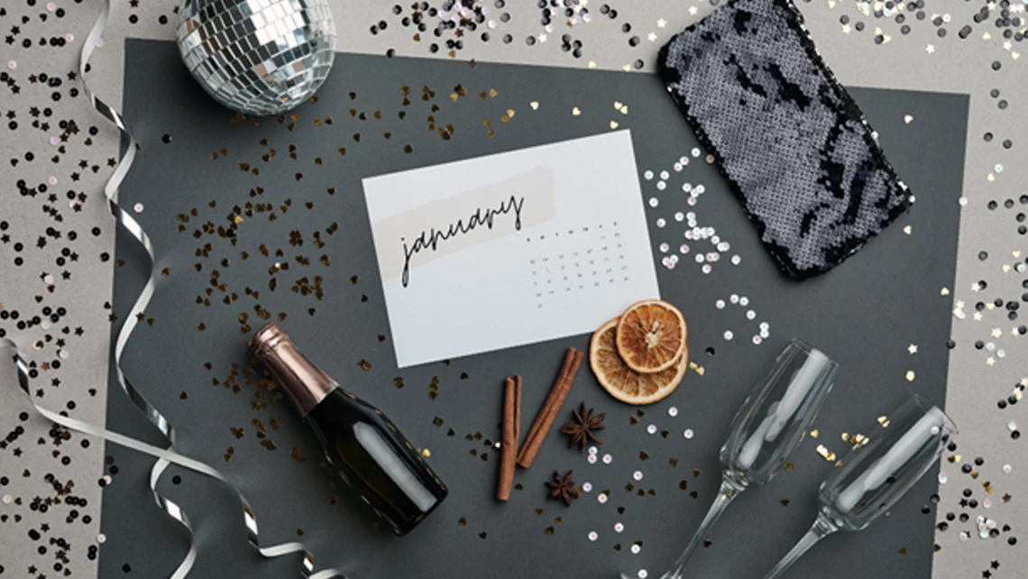 January calendar surrounded by disco ball, champagne glasses, pouch, wine bottle, oranges, cinnamon