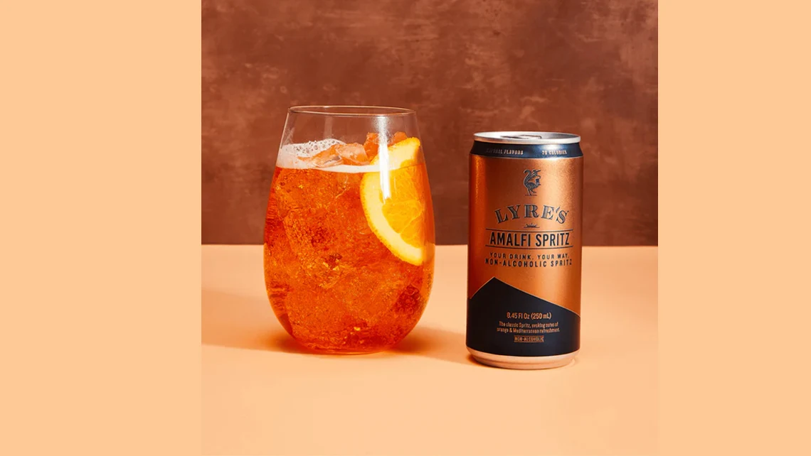 a can of Lyre’s Amalfi Spritz beside a glass of the orange spritz with a lemon wedge garnish