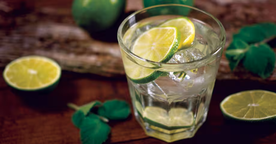 a glass of SoCal soda with ice, garnished with lime wheels and surrounded by limes and mint leaves