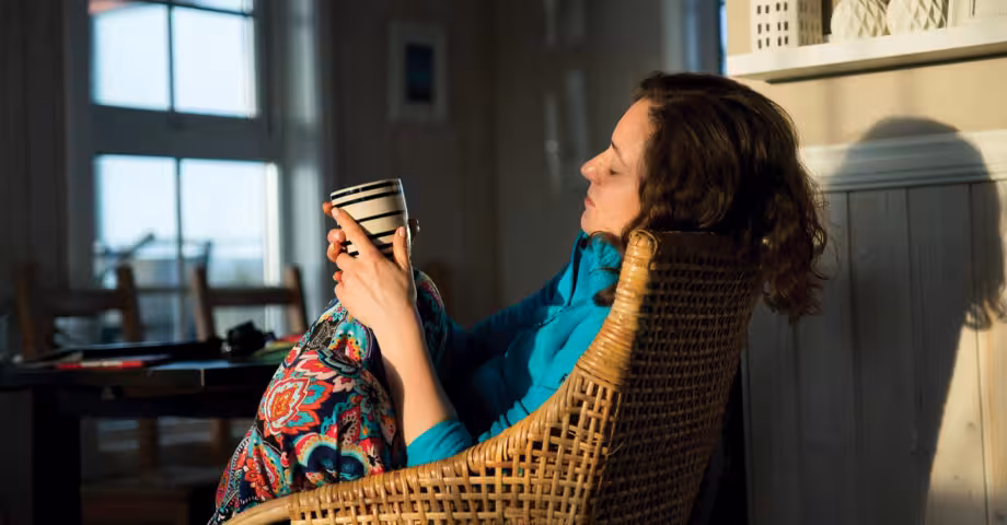 alcohol-free woman curled up in a rattan chair staring at the ceramic glass she’s holding