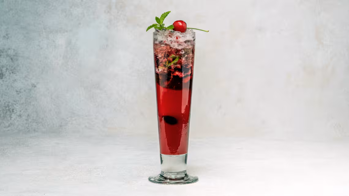 tall glass of cherry lime spritzer garnished with cherries